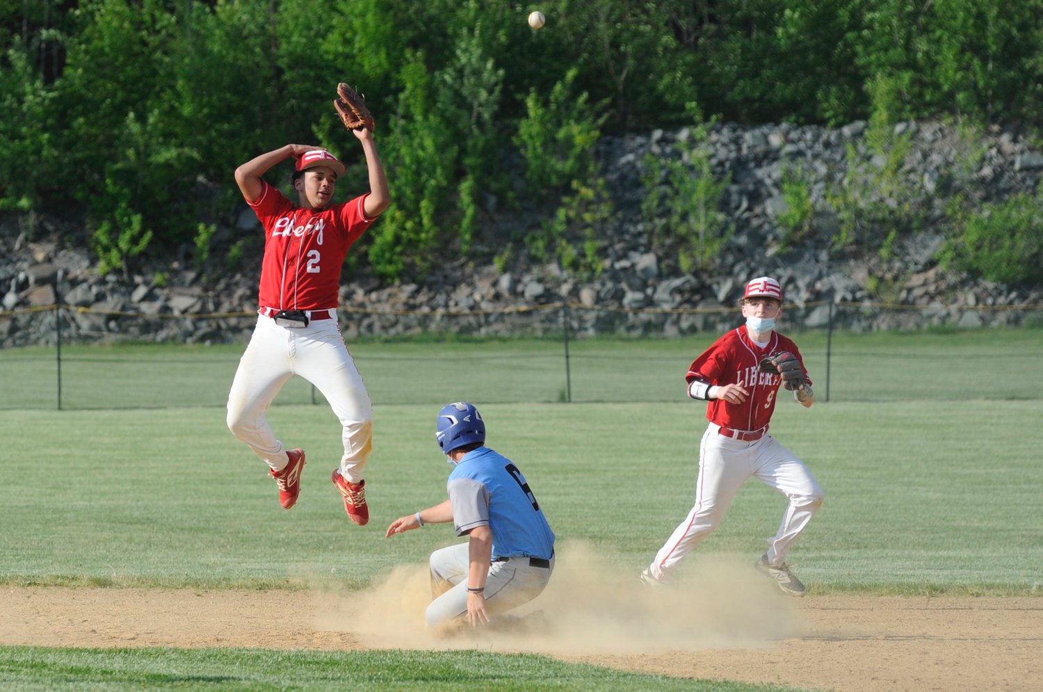 Aerobatics. Liberty’s Darlyn Jimenez gets some air under his cleats while teammate Owen Siegel reacts to Sullivan West’s Gavin Hauschild safely sliding into second on an overthrow from third.